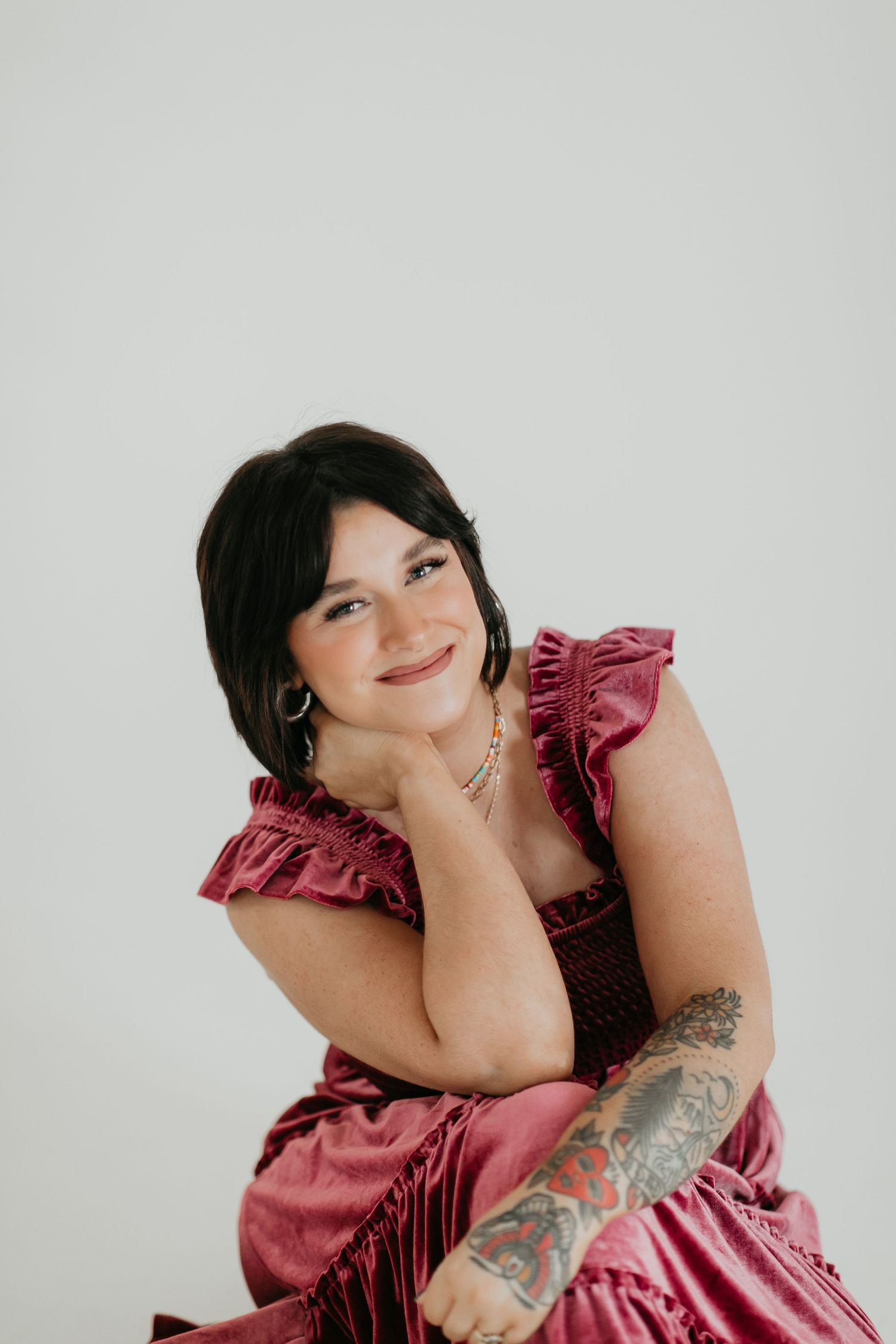 Portrait in pink ruffled dress with visible tattoo against white background.