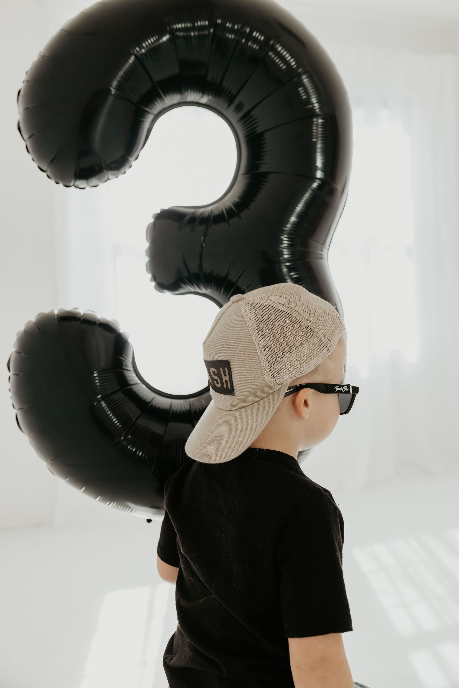 Child wearing black shirt and baseball cap with large number 3 balloon.