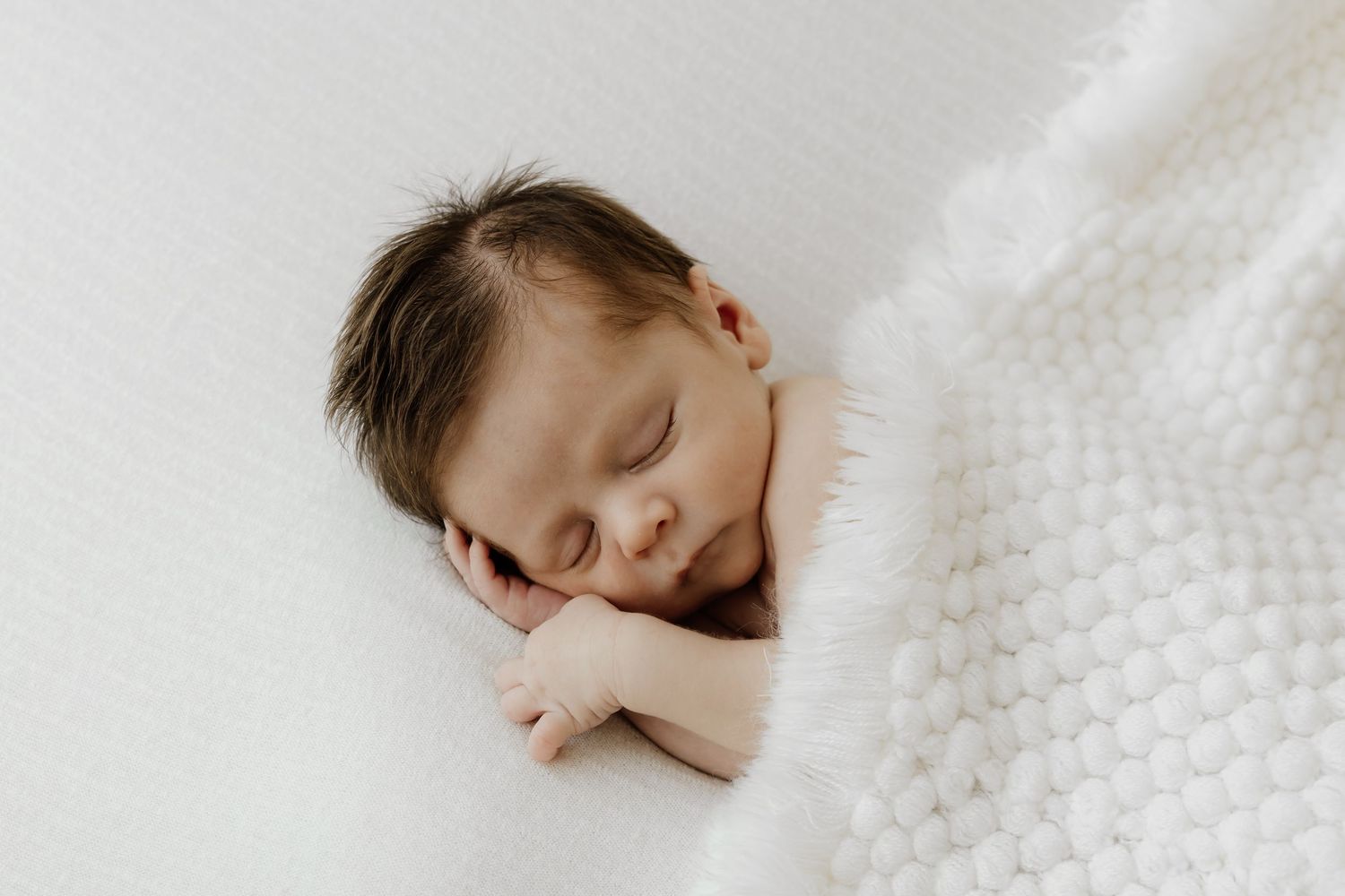 Peaceful sleeping baby nestled in white textured blanket.