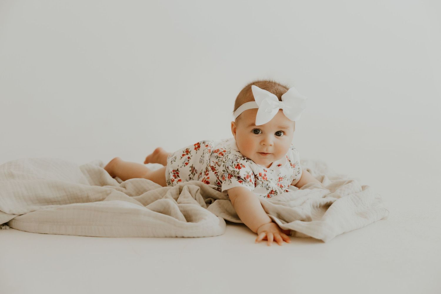 Baby lying on white blankets in a minimalist setting.