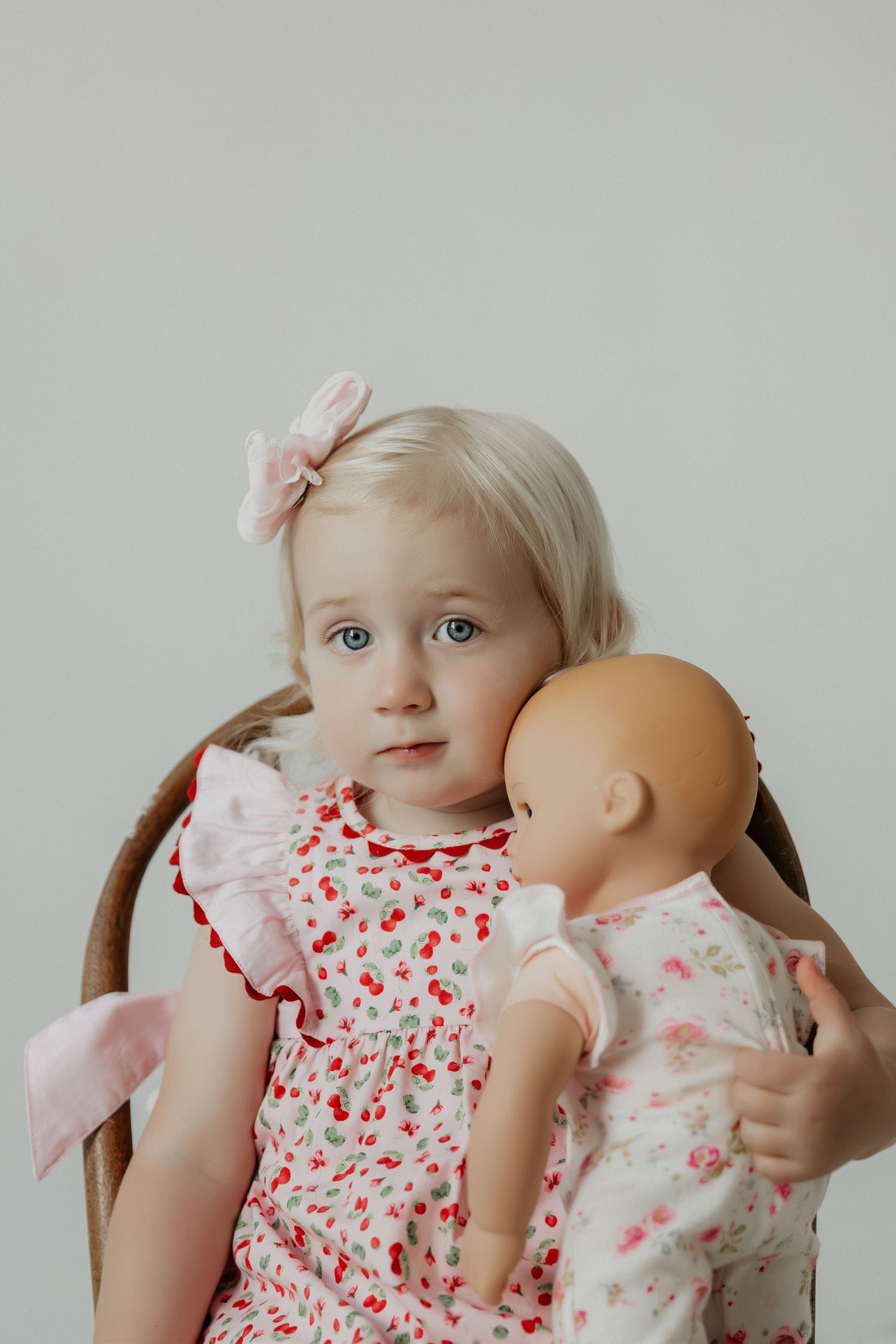 Child poses with baby dolls while wearing floral print dress.