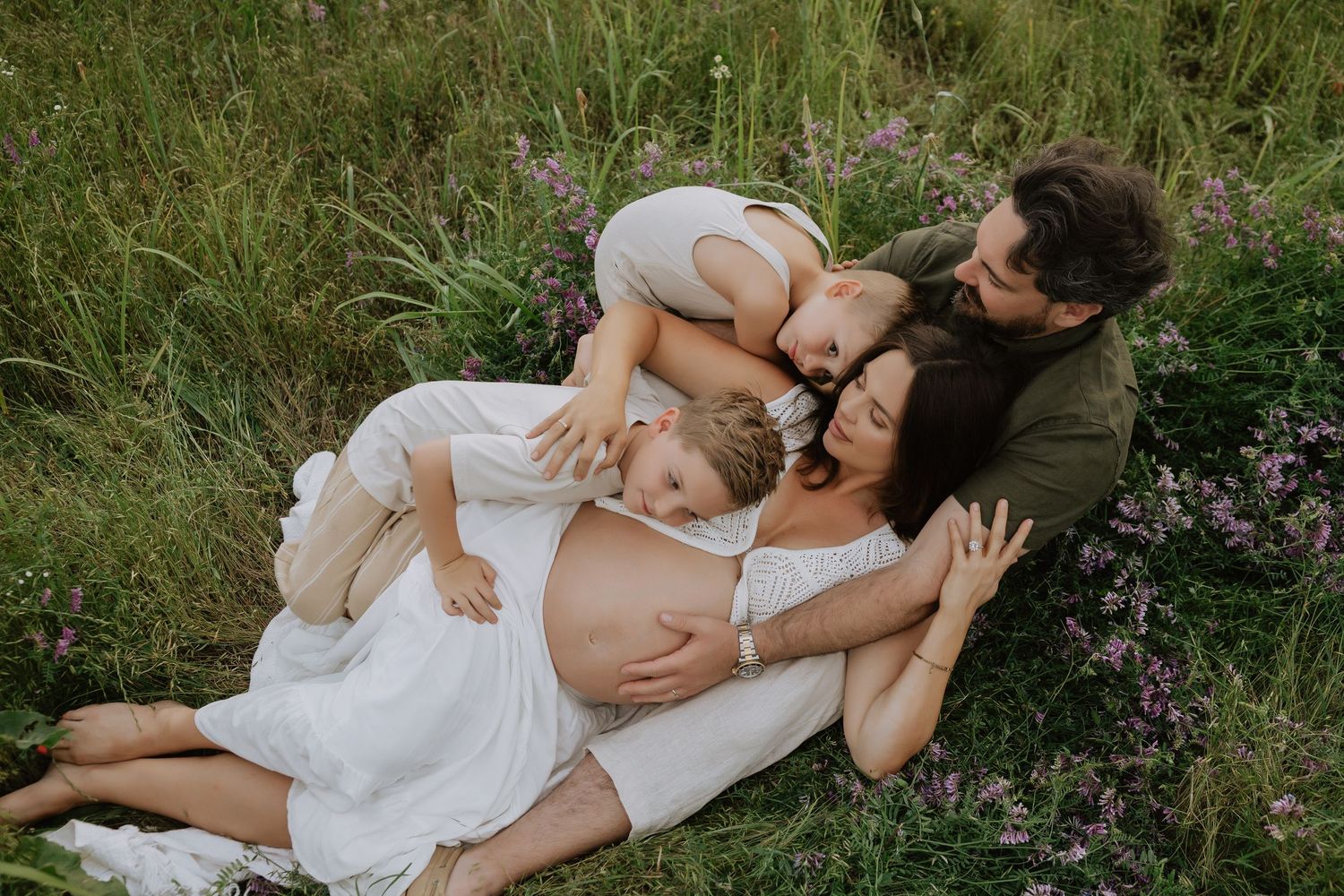 An intimate maternity moment captured in a field of purple wildflowers at sunset.
