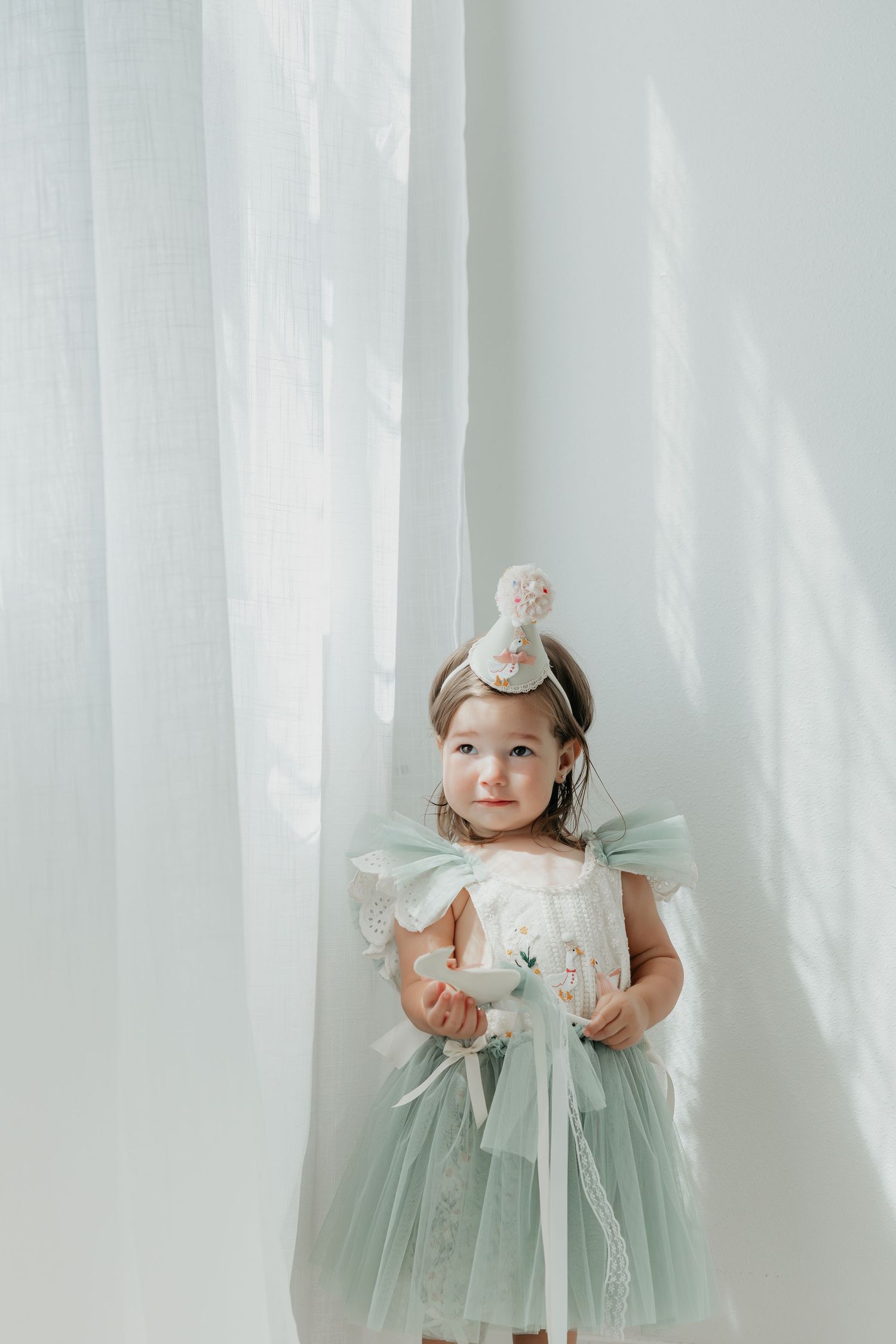 Baby in mint green tulle dress posing against white curtain backdrop.