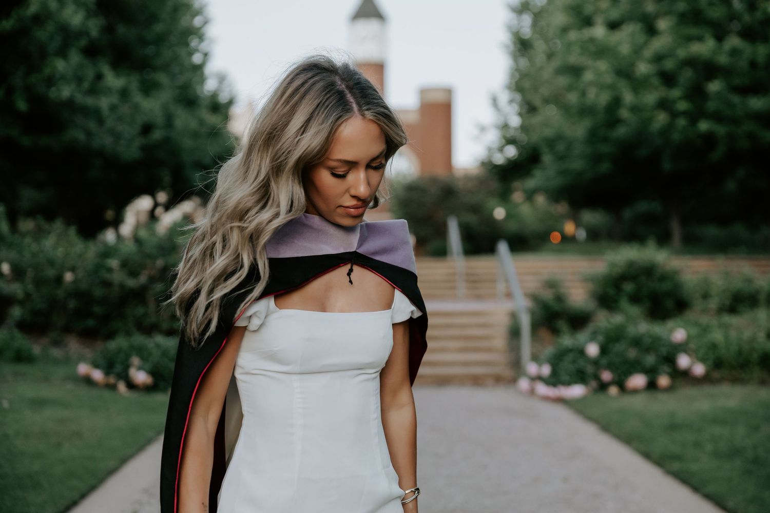 Person in elegant white dress stands in front of landscaped garden path.