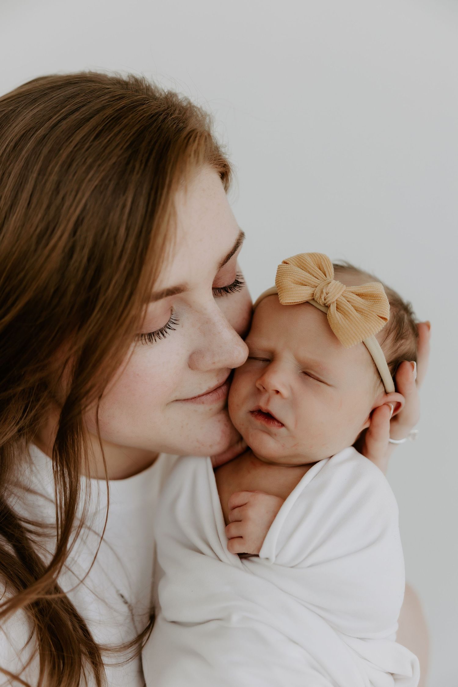 A tender moment between caregiver and sleeping newborn wrapped in white.