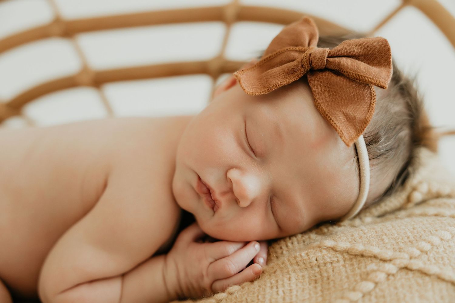 Sleeping baby wearing brown bow headband on textured surface.