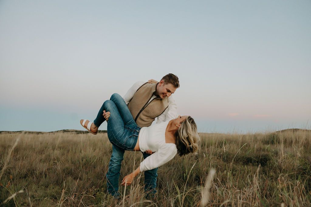 A playful couple poses in a field during sunset.