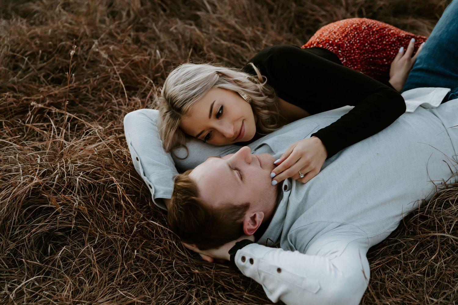 A couple lies together in tall grass during an intimate photo session.