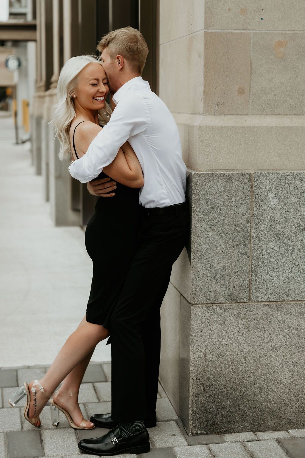 Romantic couple in formal wear sharing playful moments by stone building.