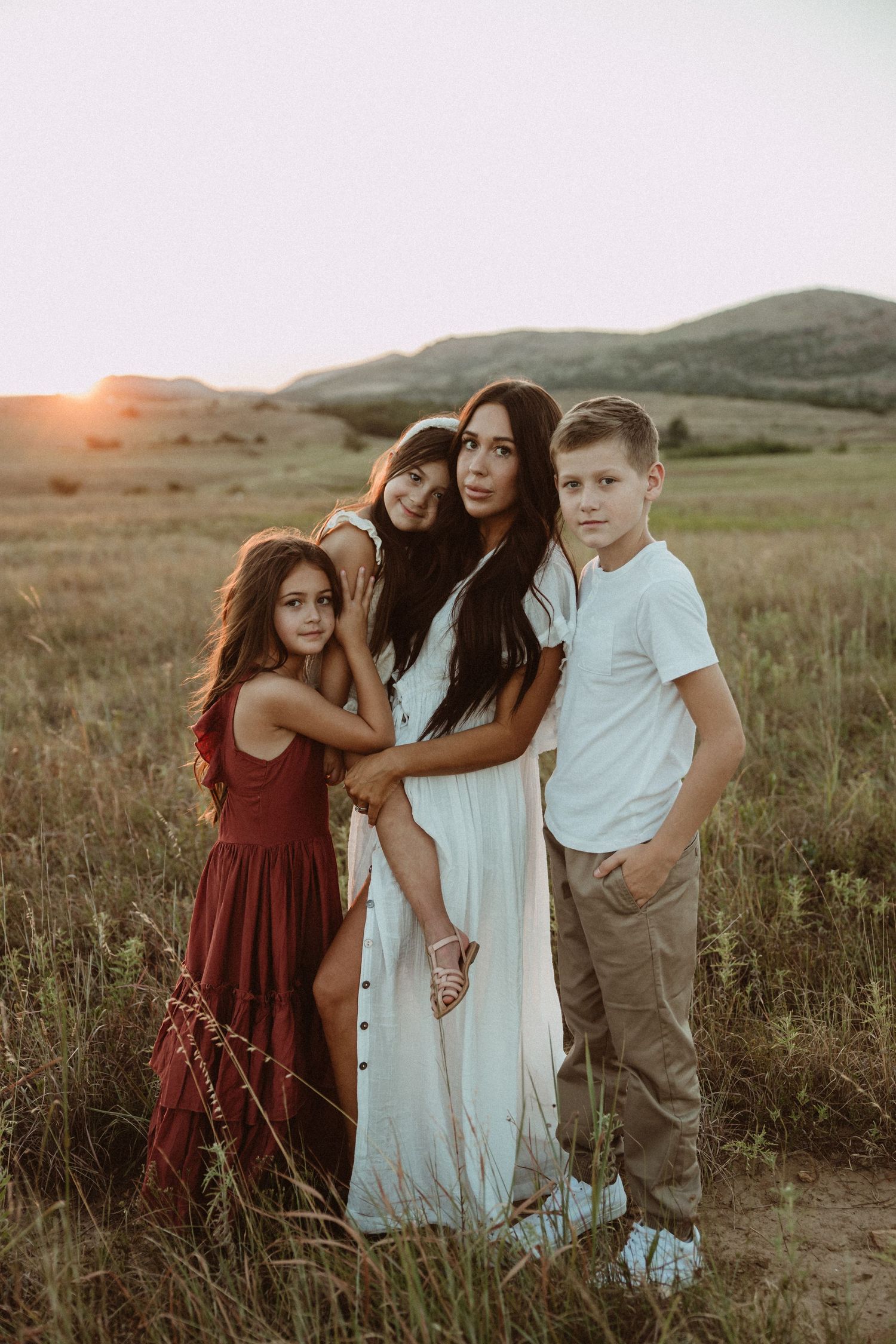 A group poses together in coordinated white and burgundy outfits at sunset in a field.