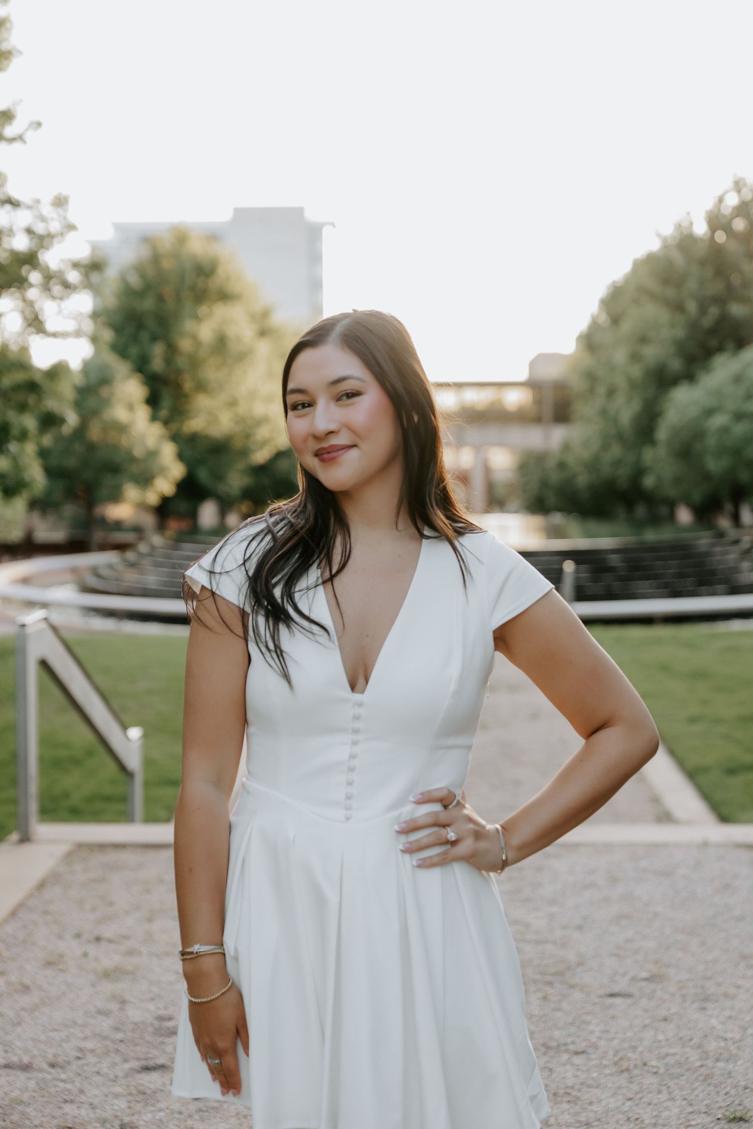 Woman in white dress poses confidently in outdoor garden setting.