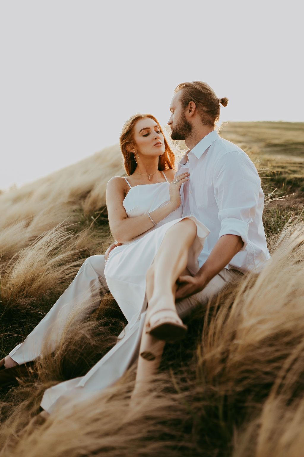 A couple embraces romantically in tall golden grass during sunset.