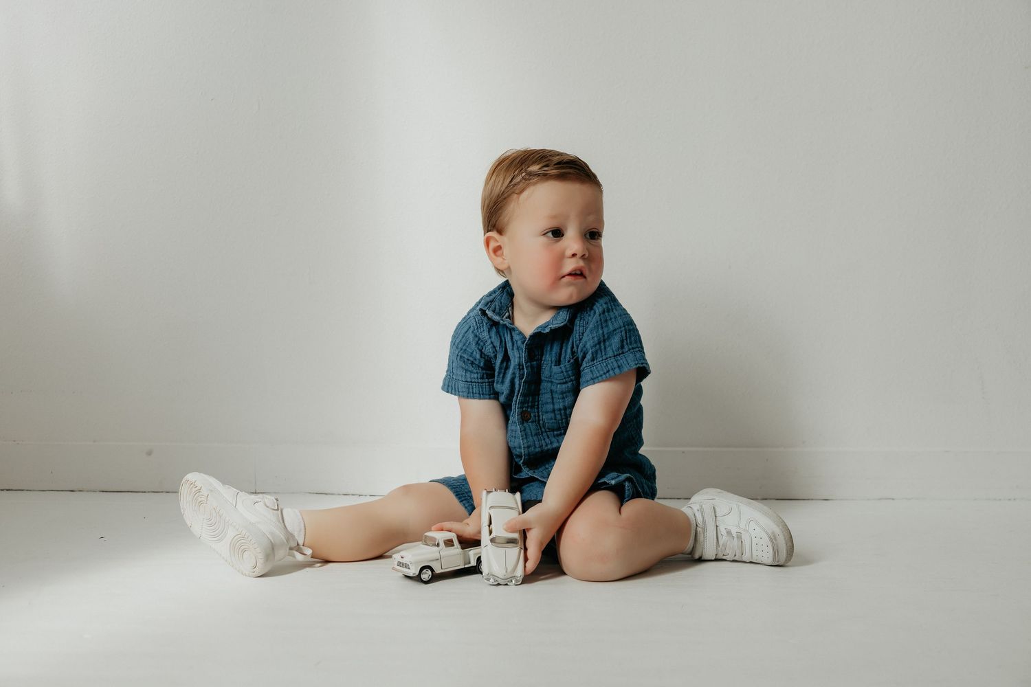 Child in blue shirt sits on white floor during photo session.