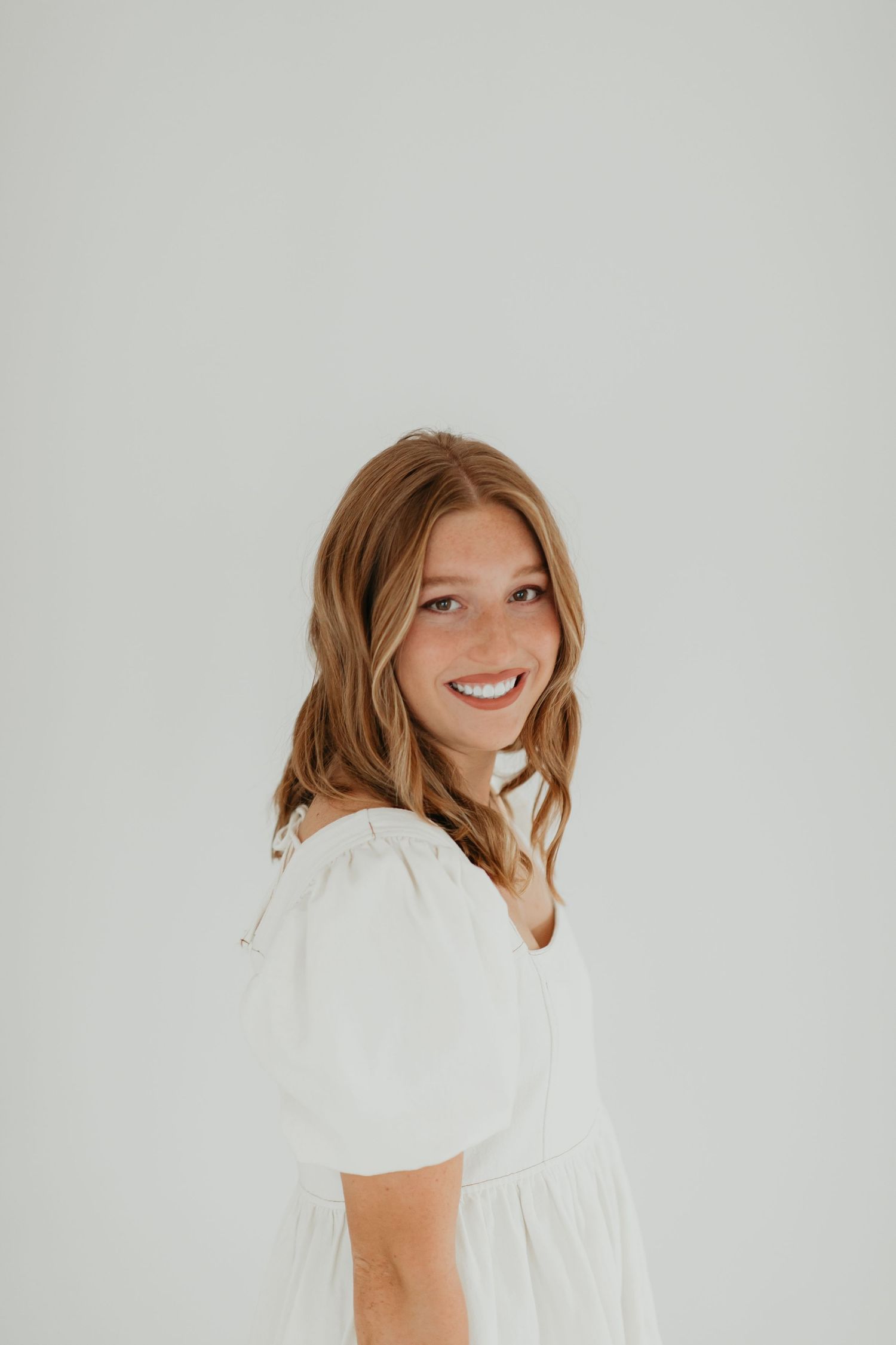 Candid portraits against white background wearing white top and pearl necklace.