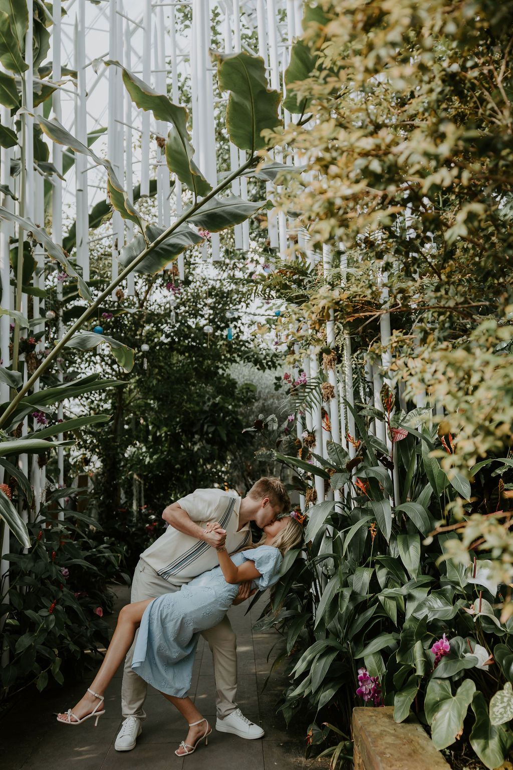 Couple sharing romantic moments among tropical plants in glass greenhouse.