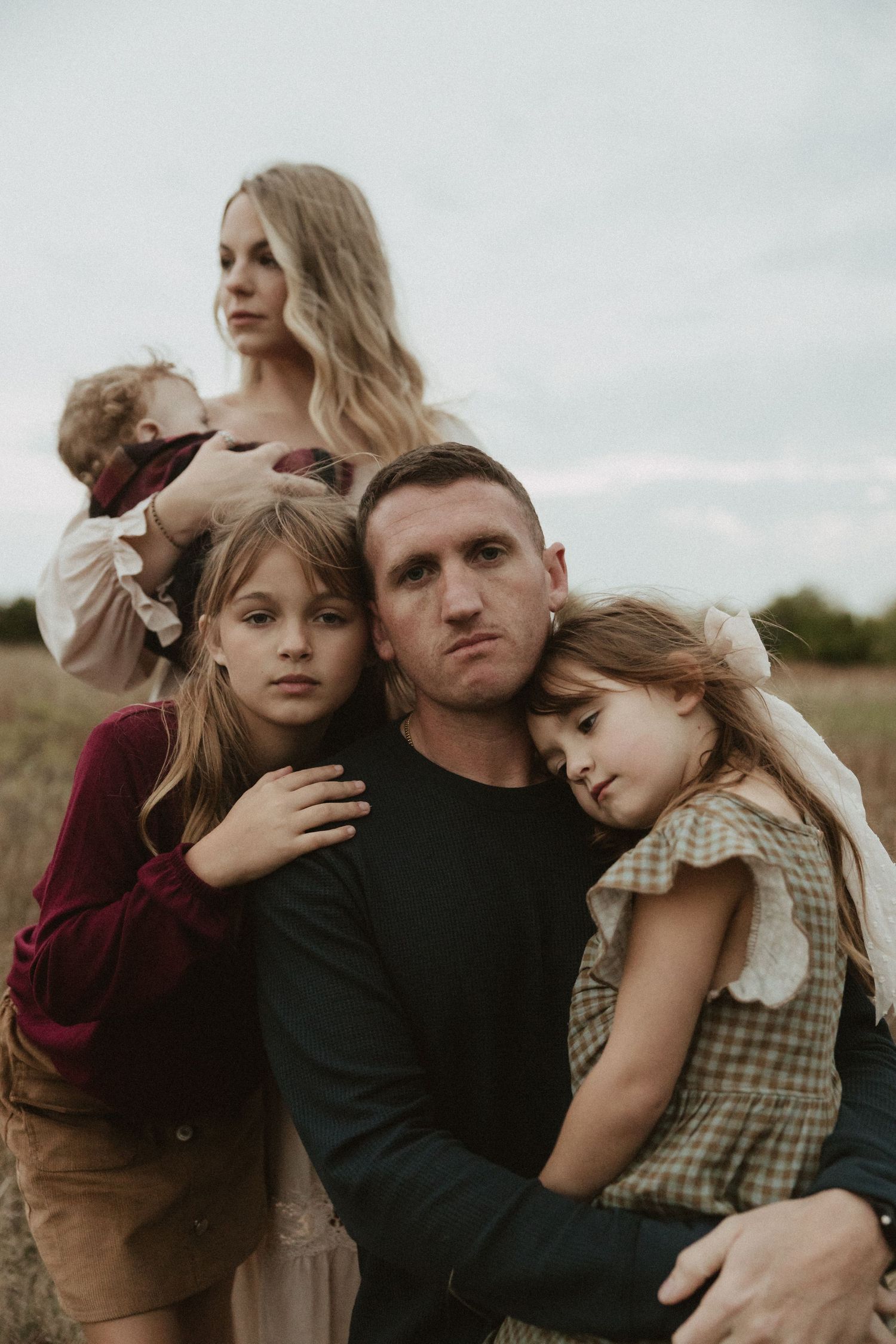 Family embracing in casual attire against cloudy sky backdrop.