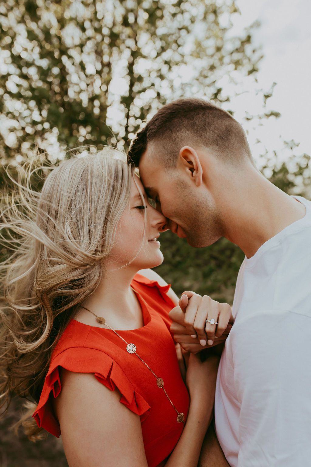 Intimate couple portrait with woman in red dress against natural backdrop.