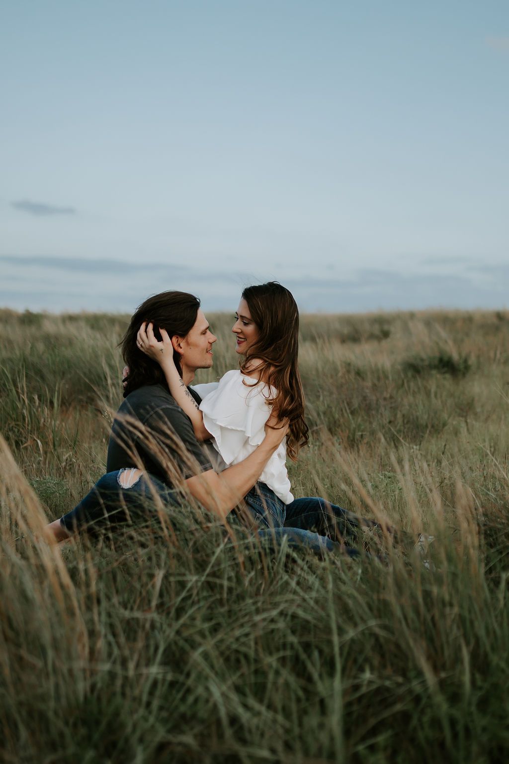 Romantic couple lying in tall grass field during golden hour photoshoot.