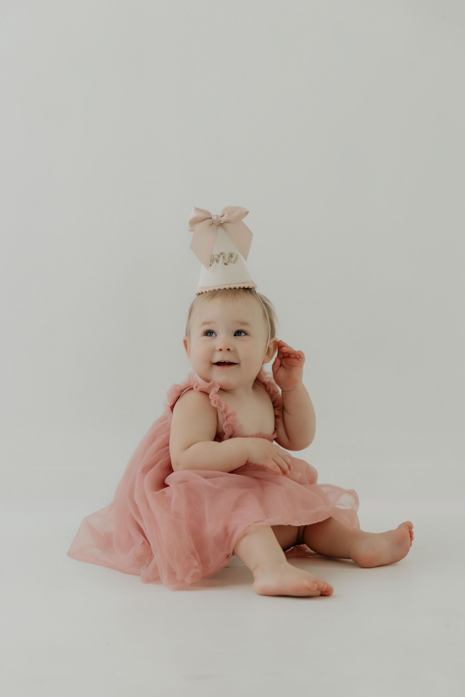 Baby in pink tulle dress against white backdrop during studio photo session.