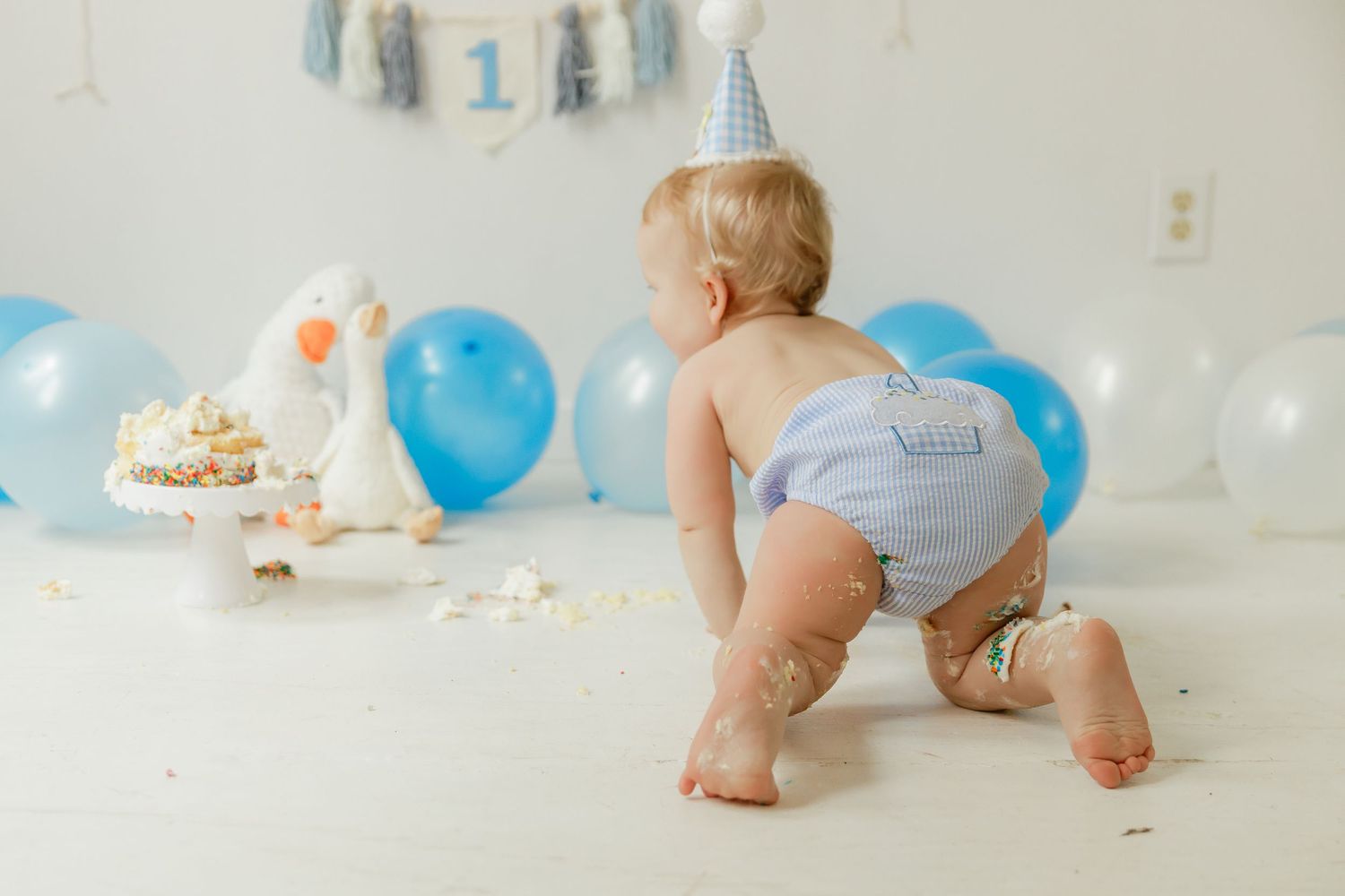 Cake smash photo session aftermath with scattered frosting and blue party decorations.