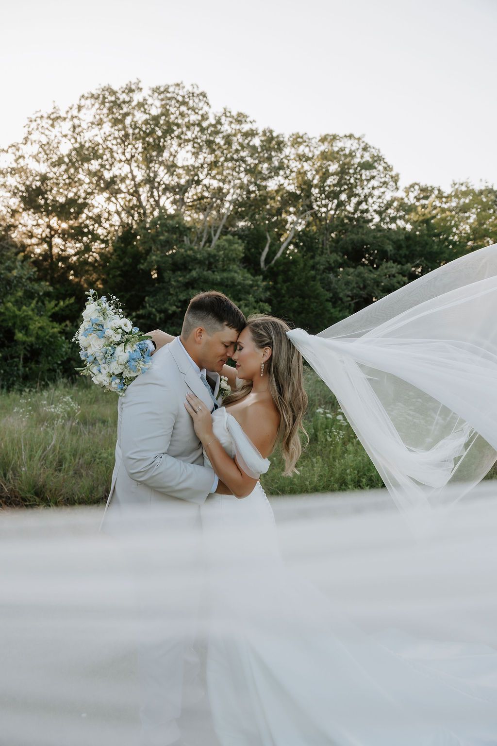 Romantic wedding portraits with flowing veil against natural landscape at sunset.