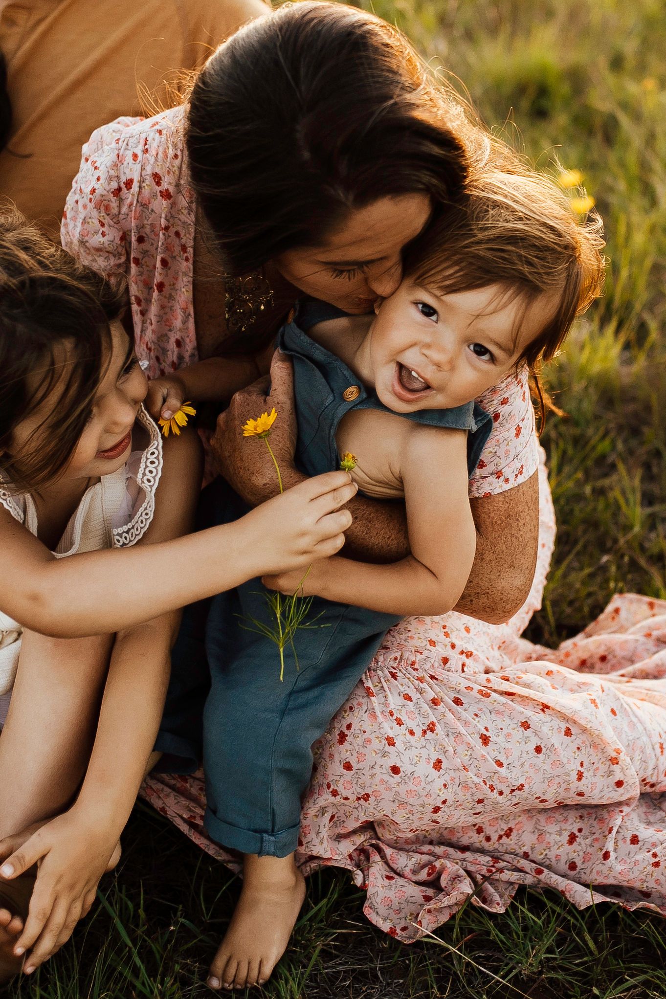 Family sharing playful moments together on grassy field in warm sunlight.