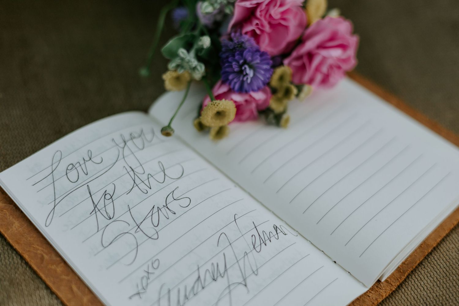 Wedding guest book with handwritten notes and pink flowers on rustic wooden surface.