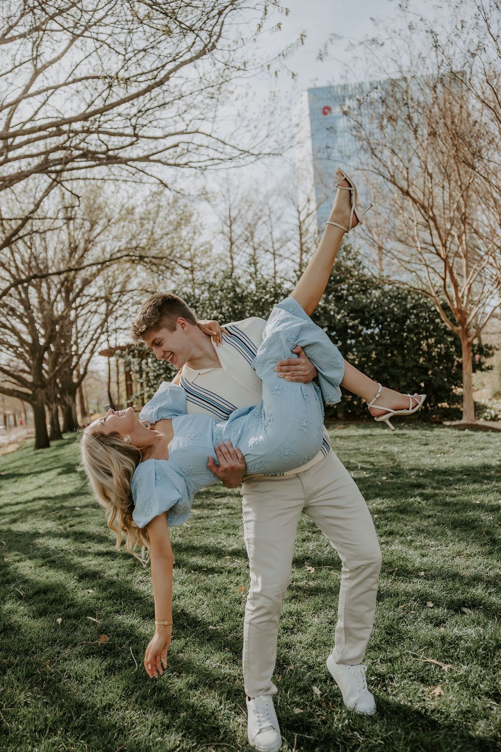 Dancing couple in casual wear performing playful dips on a sunny day in a park setting.
