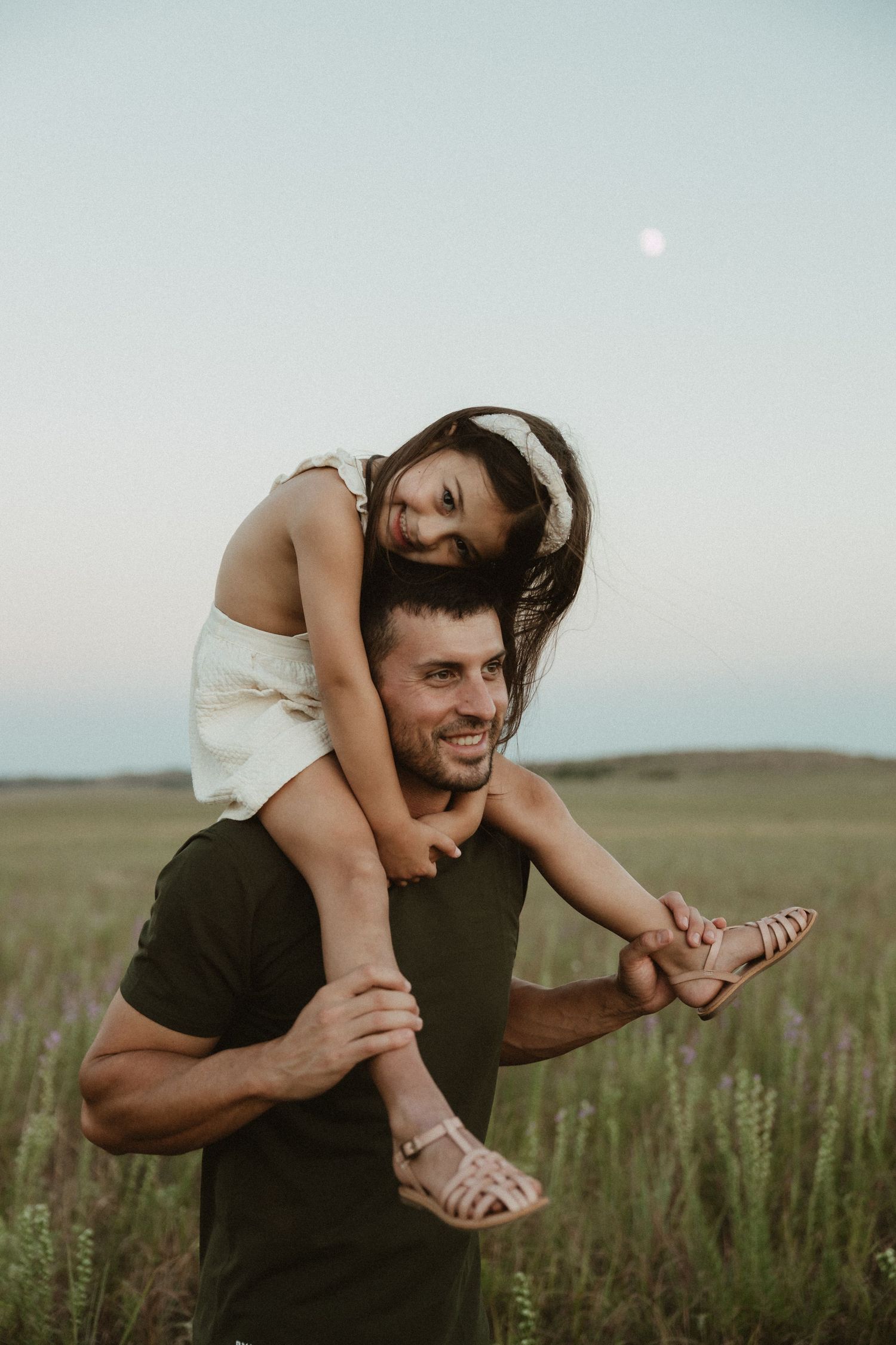 A playful piggyback ride in a field with mountains in the background at dusk.