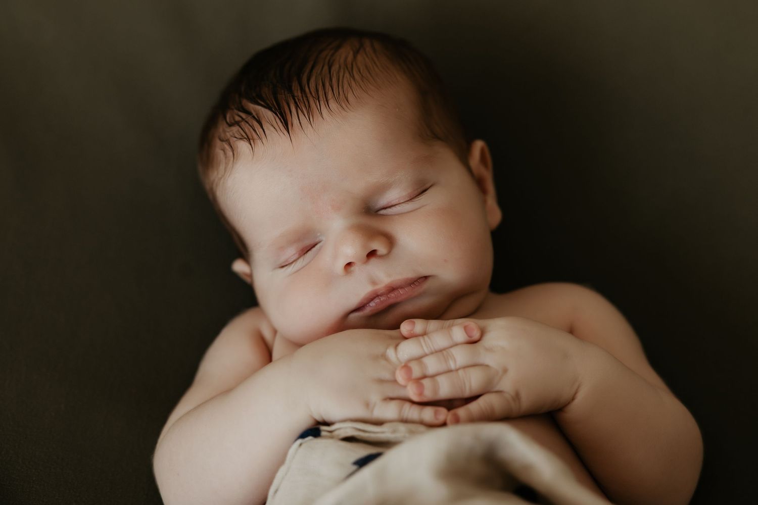 Sleeping baby wrapped in dark tones with dramatic lighting.
