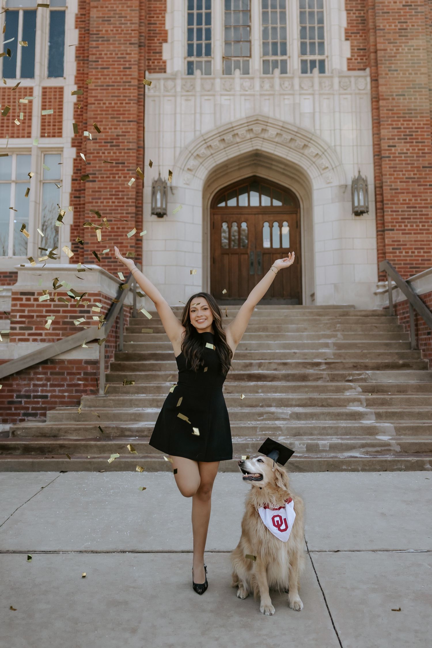 Graduate celebrates with their Golden Retriever on campus steps during graduation photoshoot.