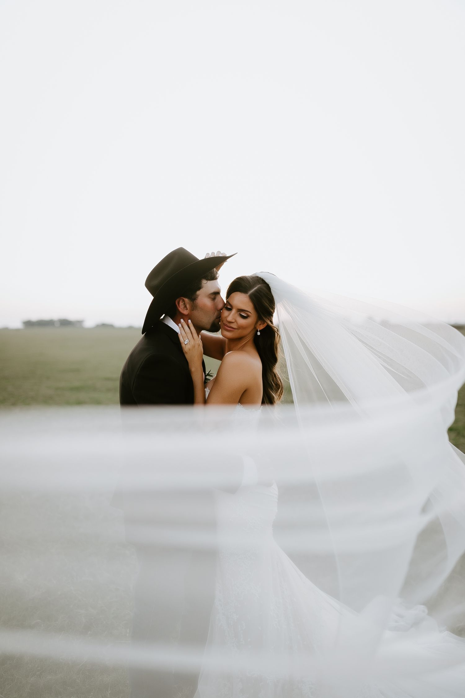 Intimate wedding moment captured through flowing white veil in outdoor setting.
