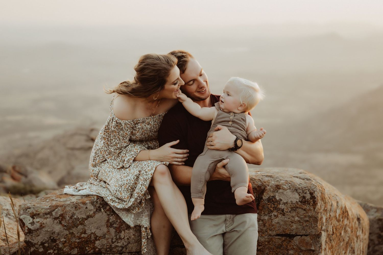 Family sitting together on stone wall overlooking scenic mountain vista.