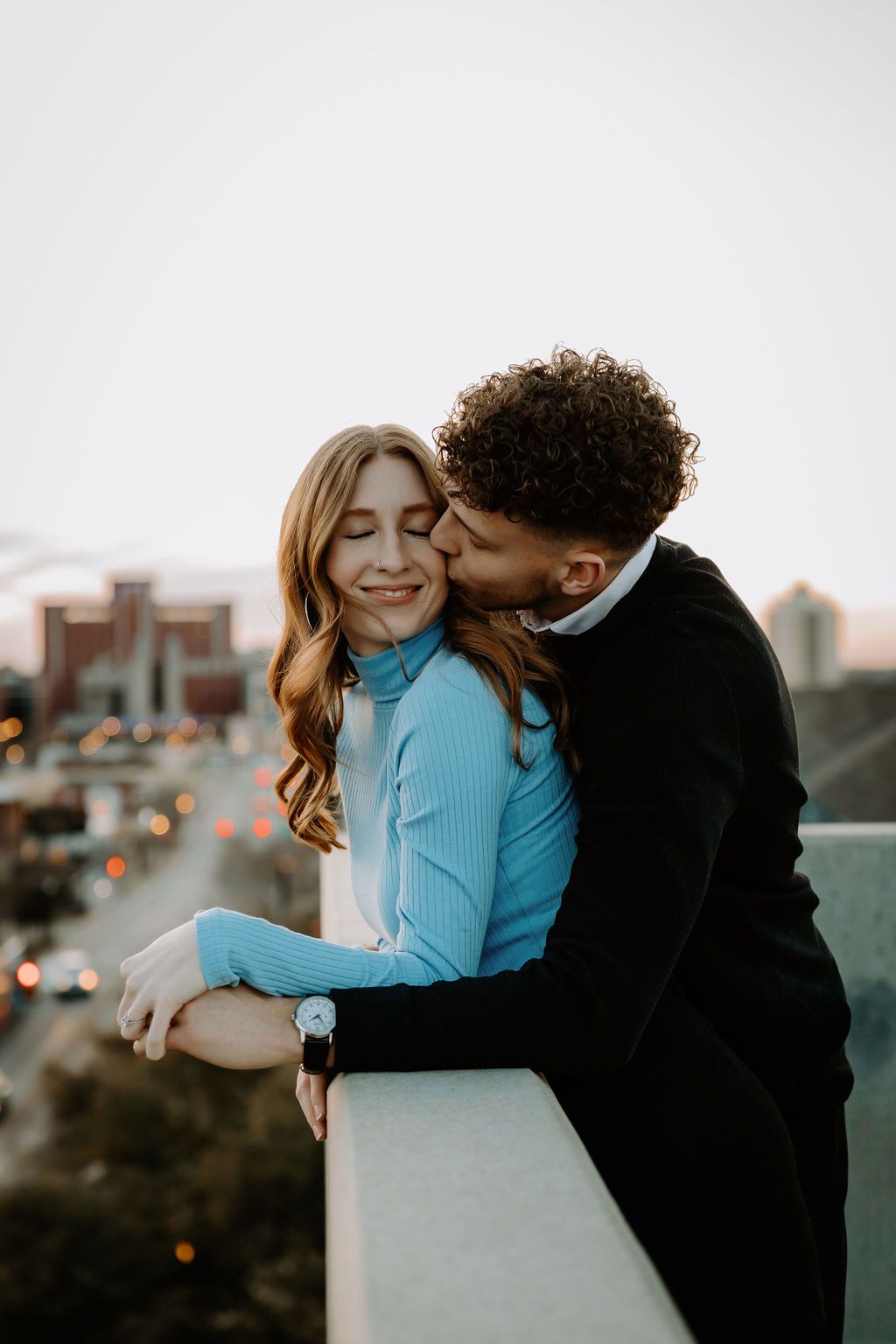 Couple embracing on rooftop during golden hour with urban backdrop.