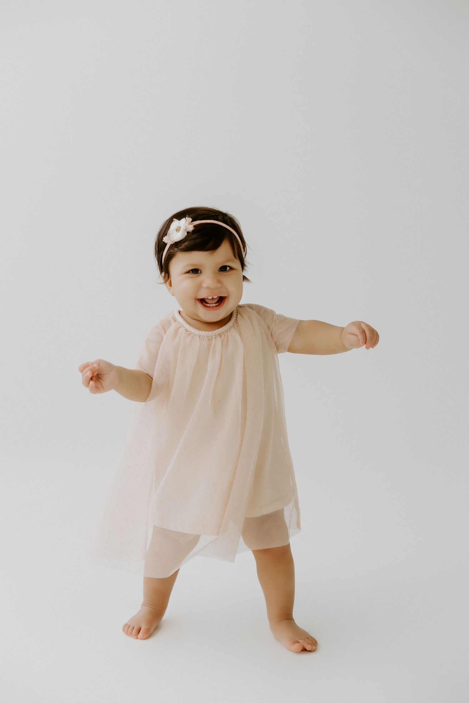 Baby in flowing peach dress dancing against white background.