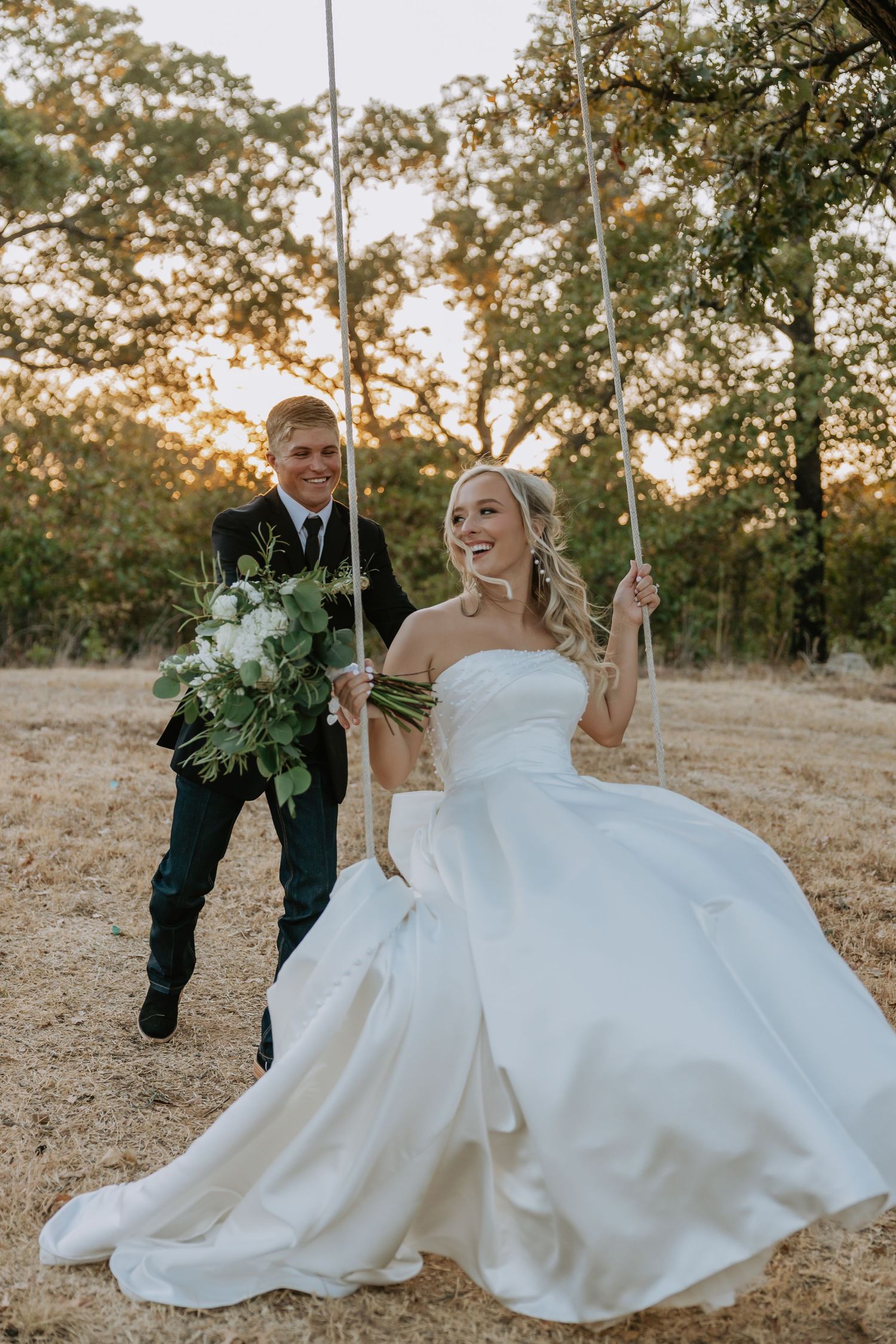 Wedding couple laughs and plays together in golden sunset field.