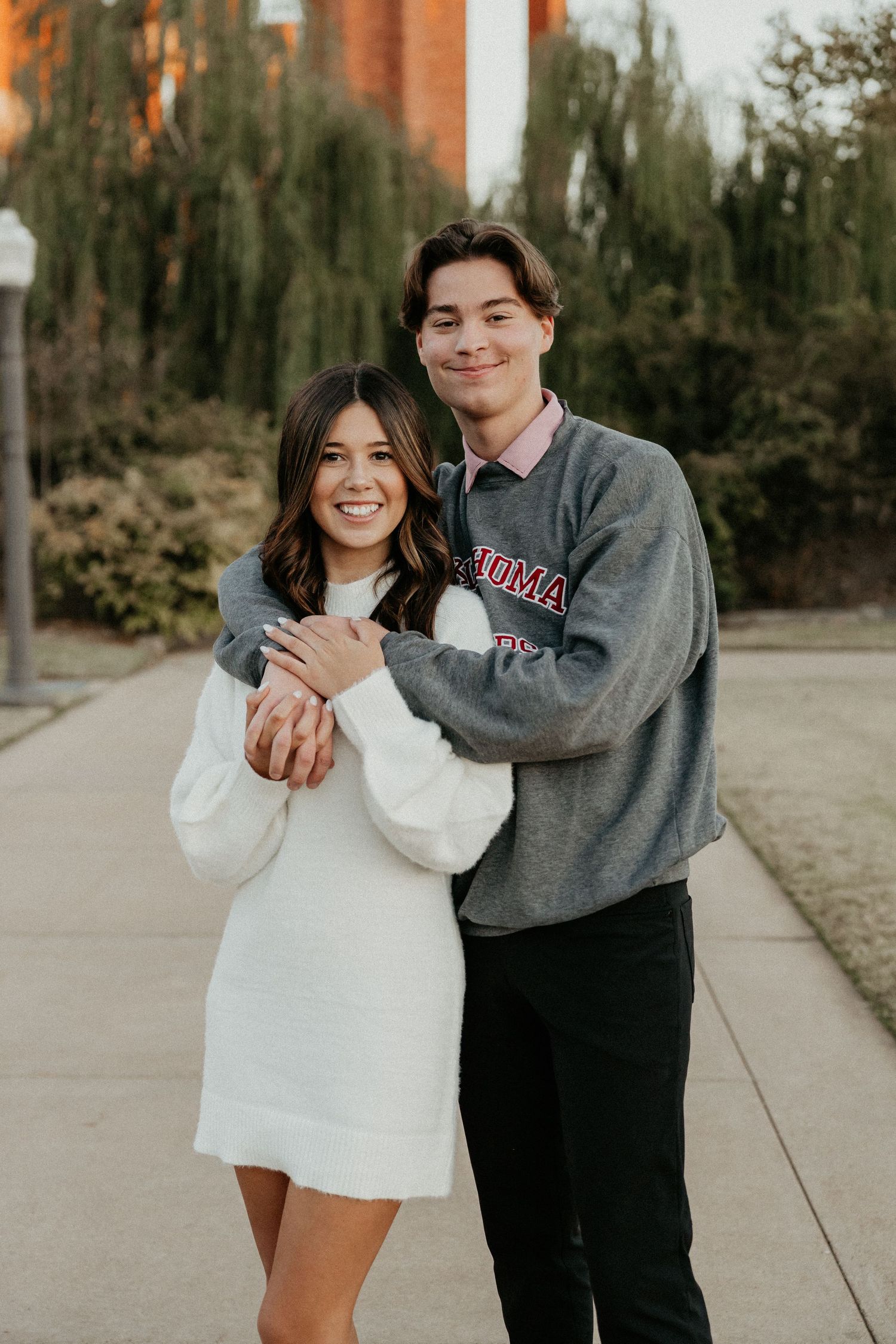 Couple in casual wear embracing and laughing together on a tree-lined path.