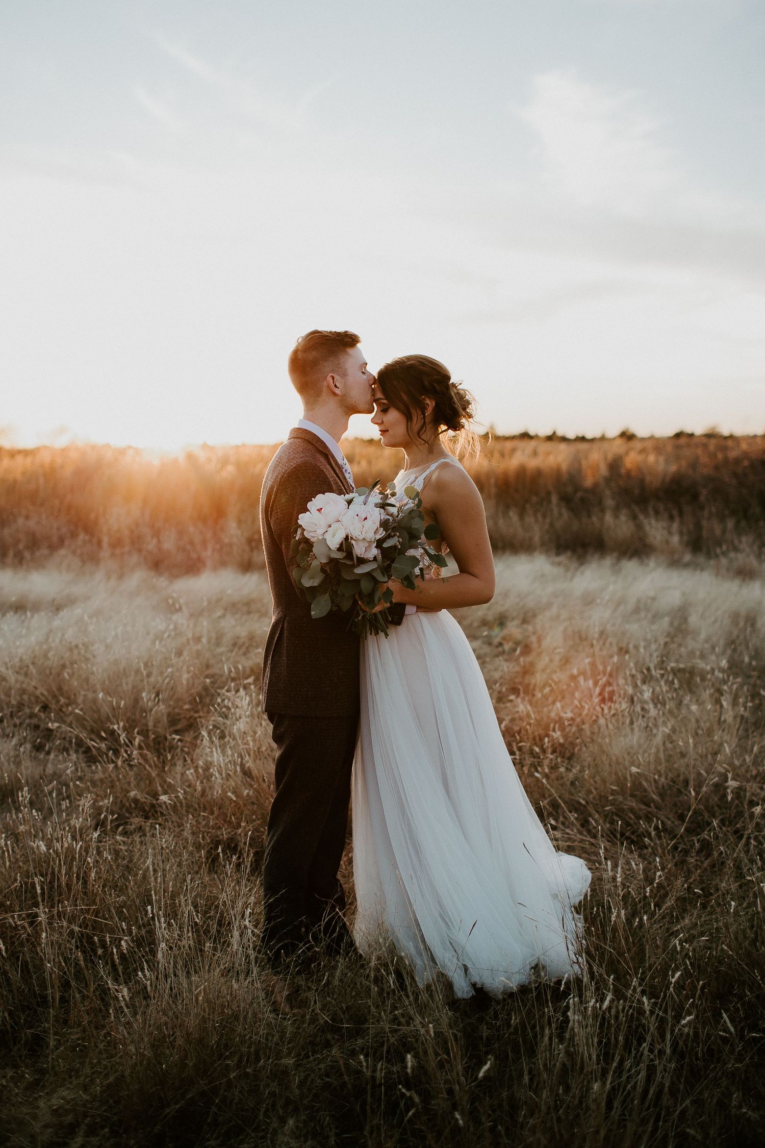 Sunset wedding portraits in tall grass field with dramatic golden hour lighting.