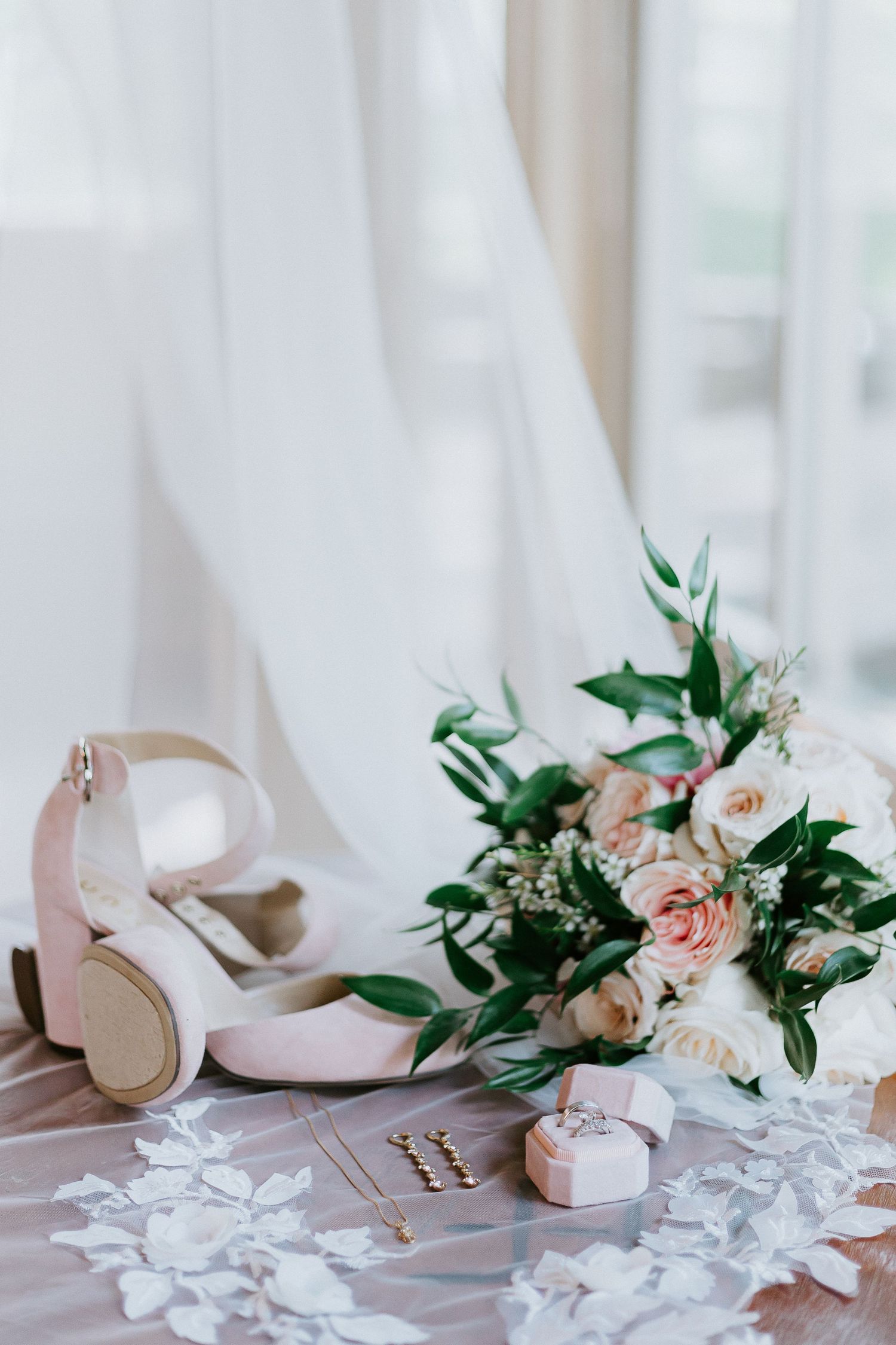 Elegant wedding accessories including pink heels and roses arranged on a white surface.