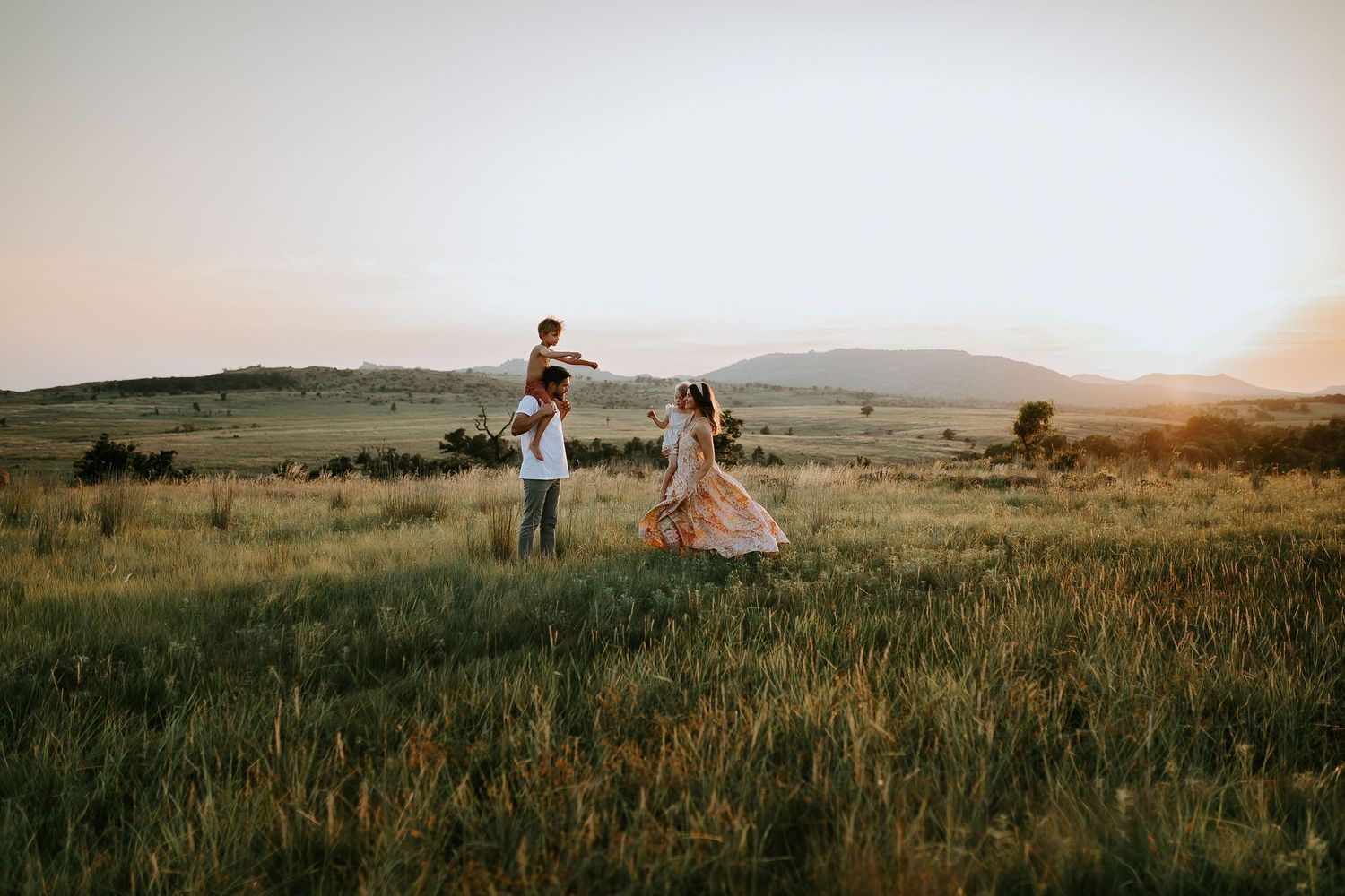 Panoramic view of people walking through a golden prairie field at sunset.