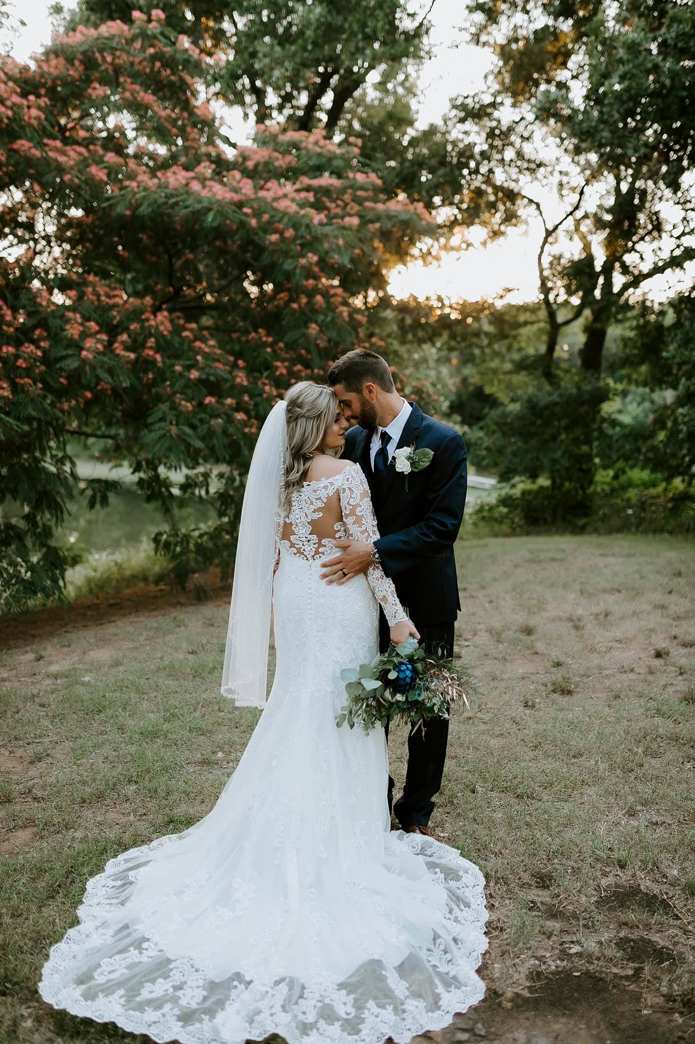Elegant wedding couple embraces on hillside during sunset.