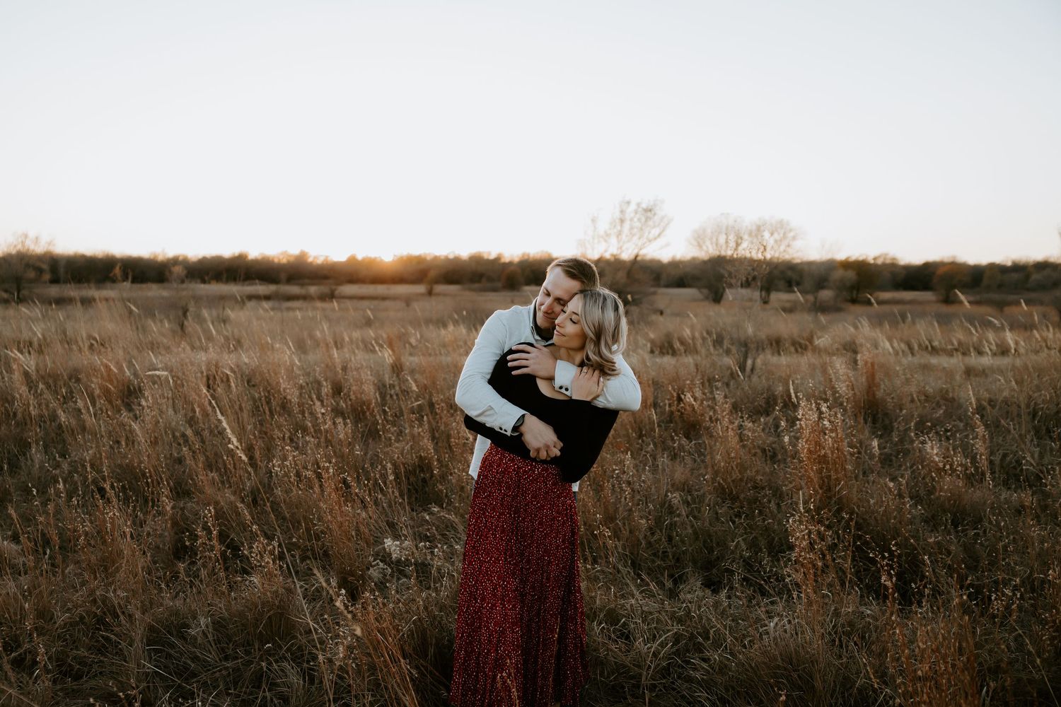 Panoramic view of a couple standing in a vast autumn field at sunset.