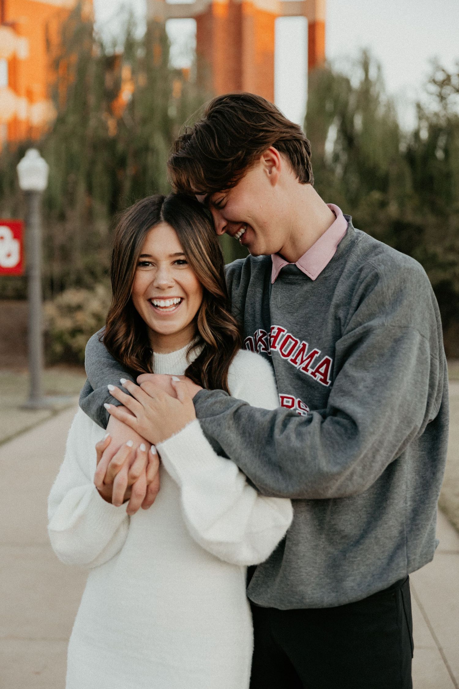 Happy couple in white sweater and grey sweatshirt sharing joyful moments outside.
