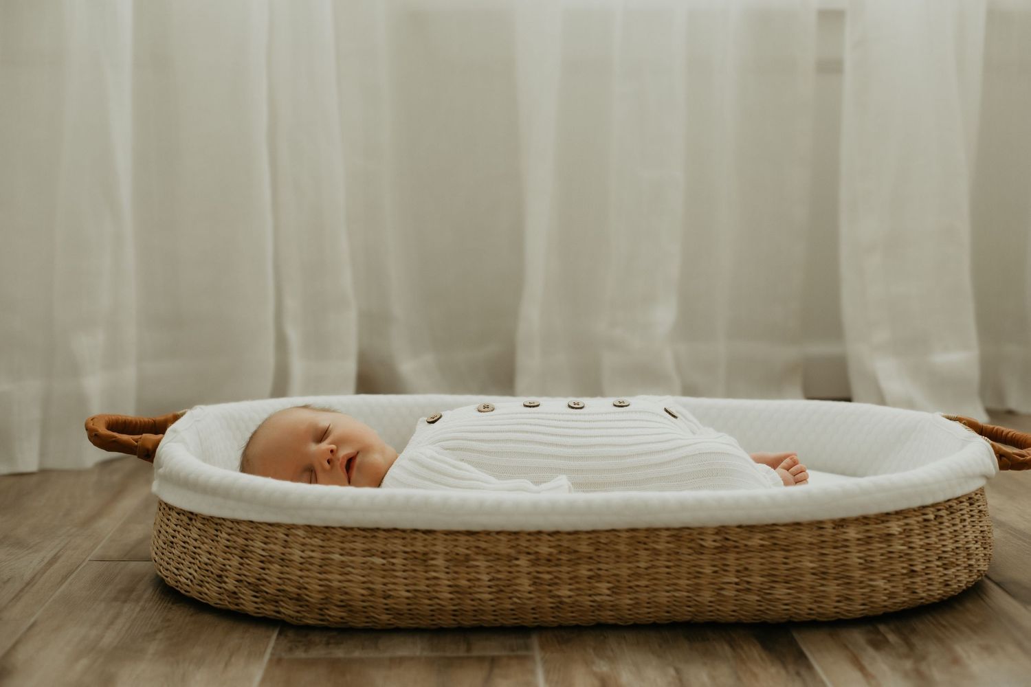 Minimalist nursery scene with woven bassinet and white curtains.
