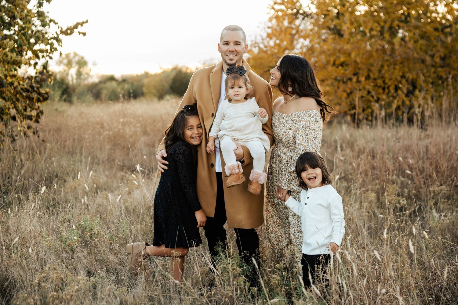 Autumn family photoshoot in a field with golden light filtering through trees.