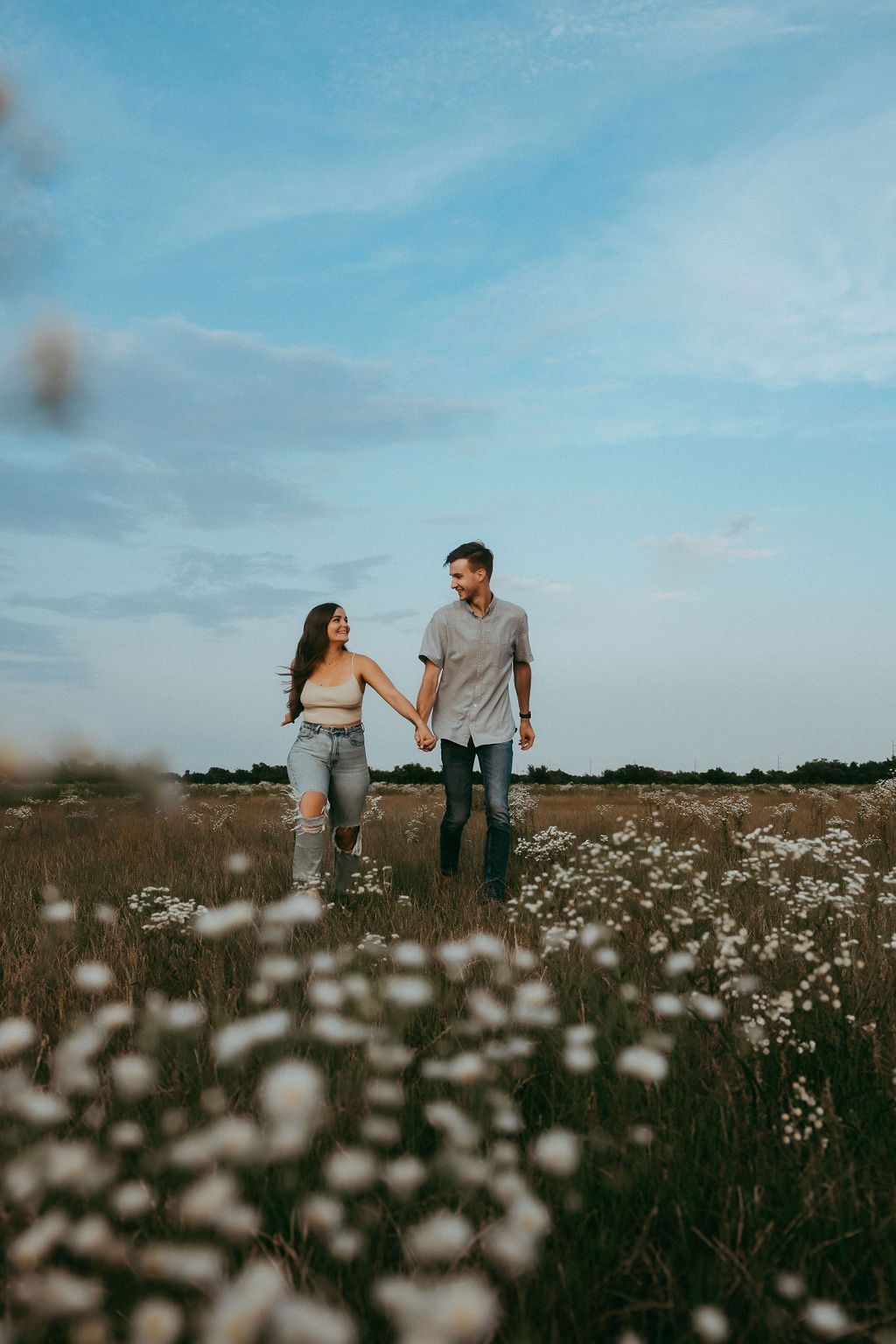 Couple walking together through a scenic field of white wildflowers under blue sky.