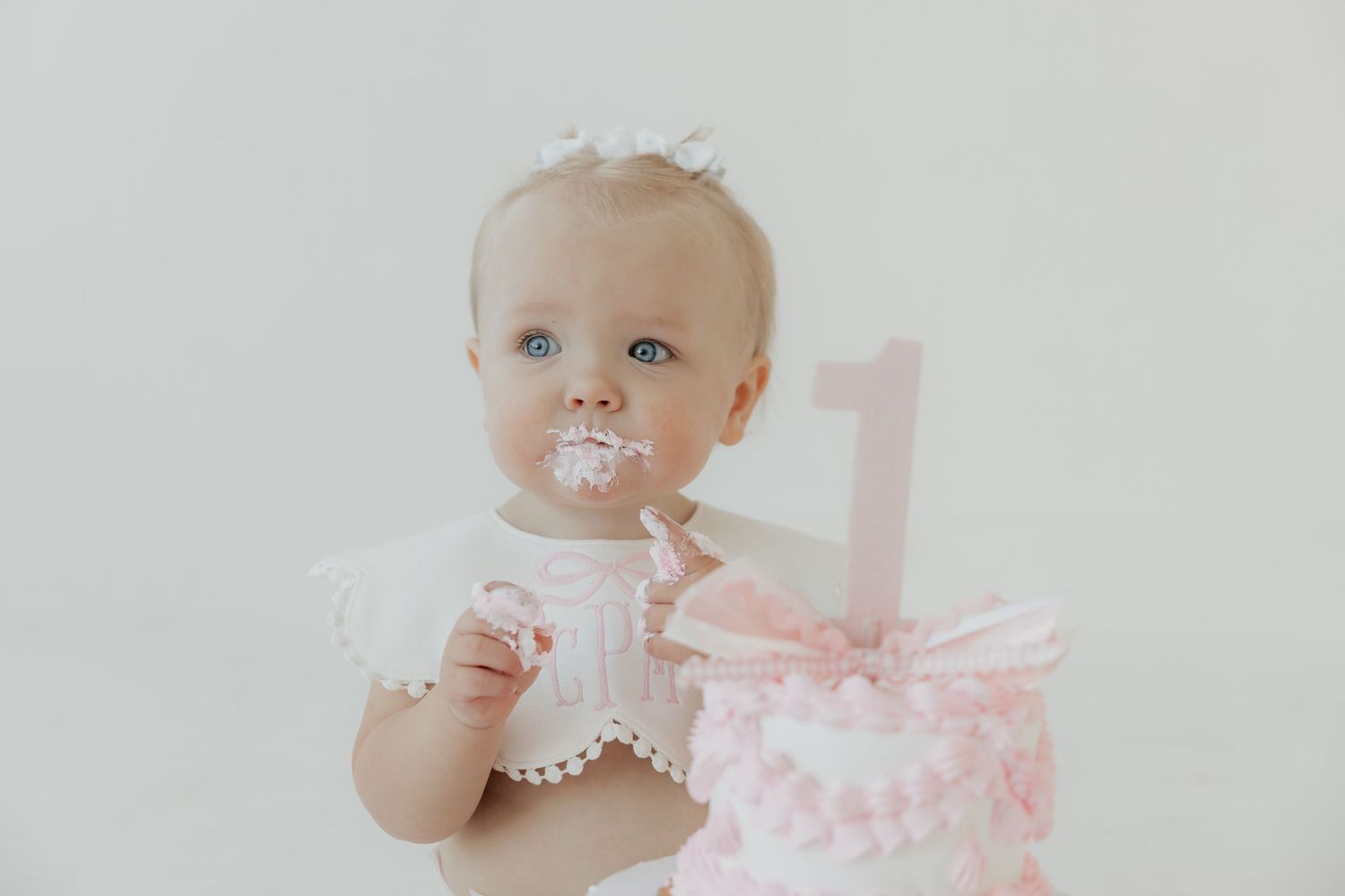 Elegant pink and white cake smash setup with pearls and soft decorative elements.
