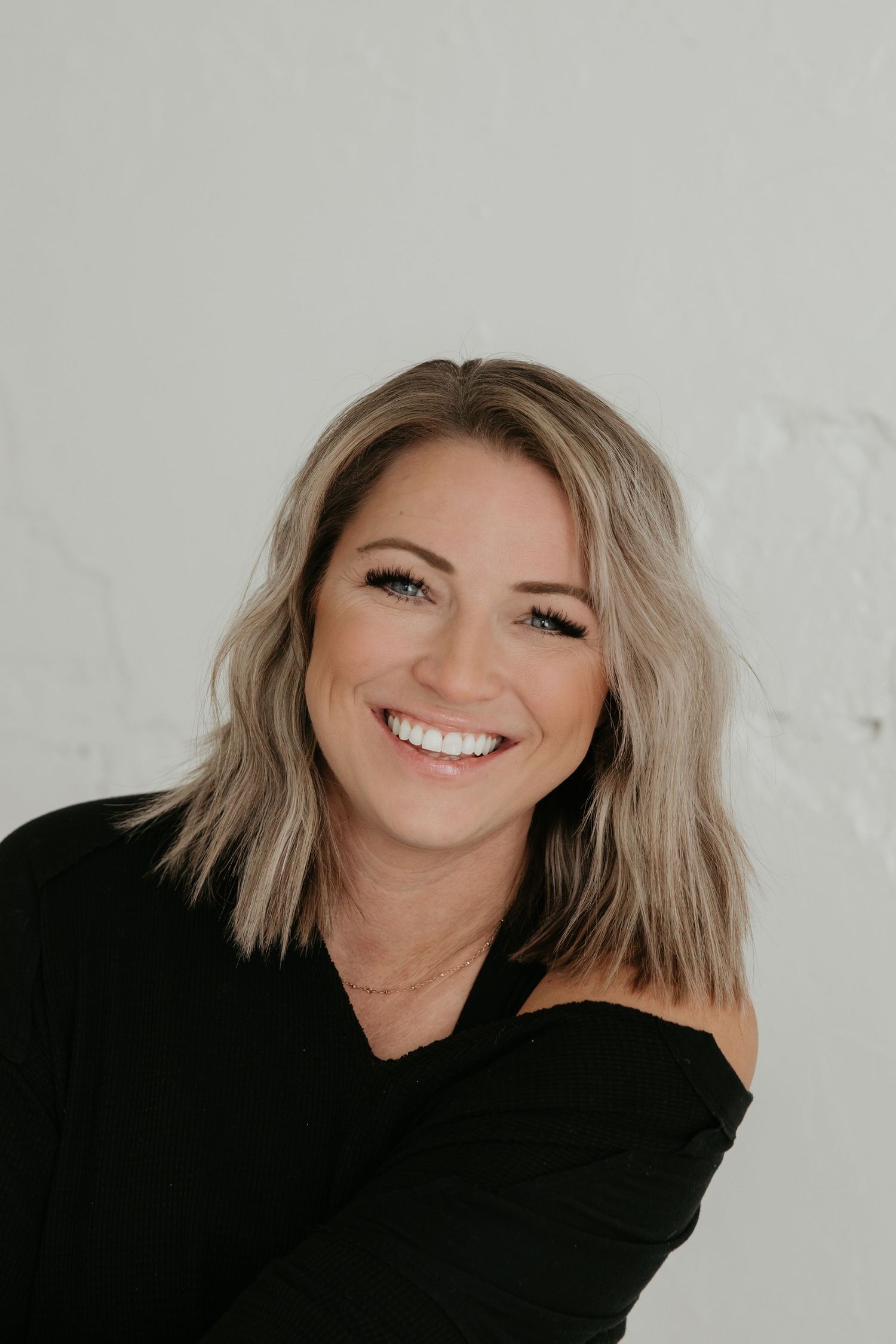 Professional headshot with blonde hair and black top against white backdrop.