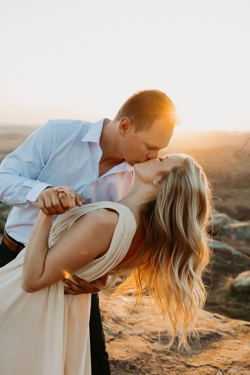 Romantic couple sharing intimate moment during golden hour sunset on rocky terrain.