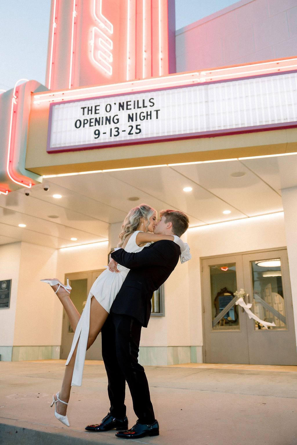 Romantic couple dancing under vintage theater marquee lights at night.